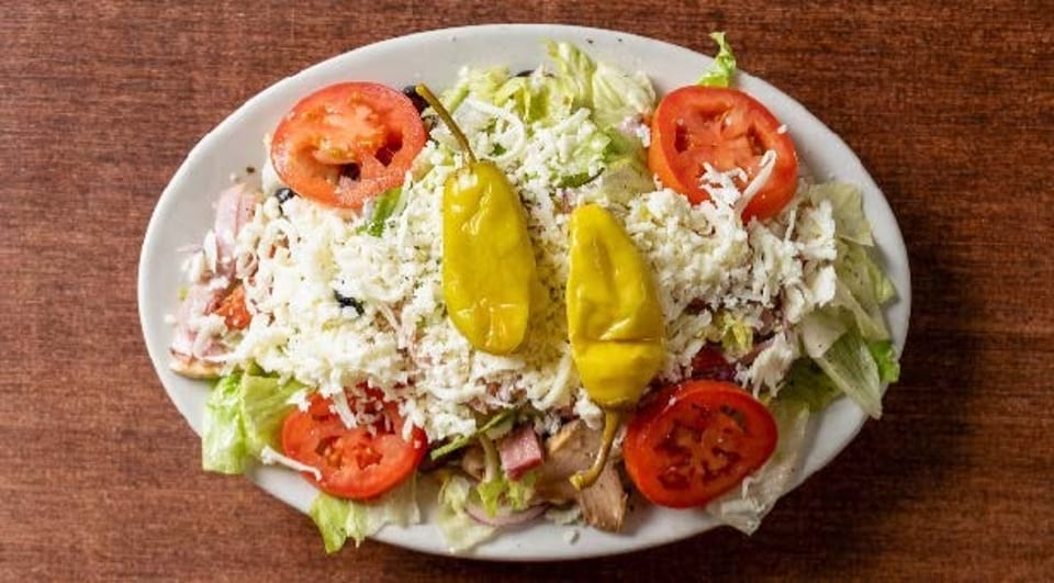 A large salad with lettuce, tomatoes, cheese, and two yellow peppers on a white plate.