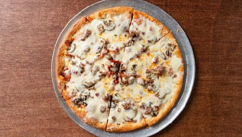 A whole white pizza with mushrooms and sausage, sliced and served on a metal pan.