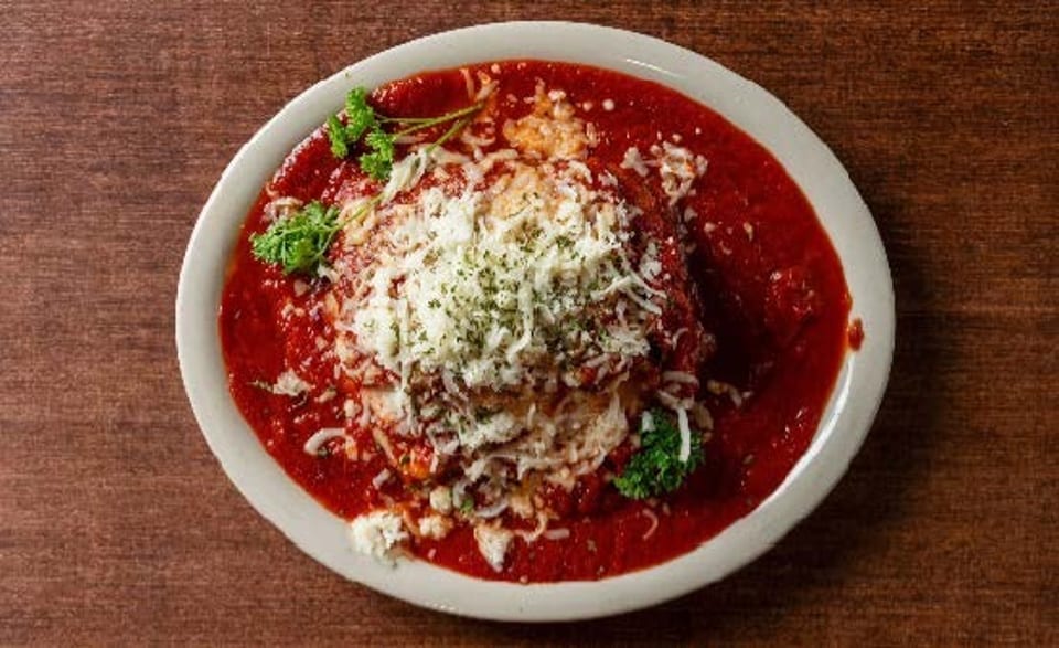 Chicken Parmesan with marinara sauce, melted cheese, and parsley on a white plate.